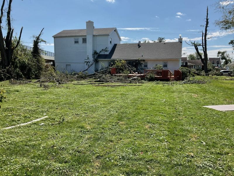 Fort Washington Tornado 11 Why I Joined a Tornado Clean Up Chainsaw Gang MyFixitUpLife Suburban backyard after a storm white two story house with a gray roof a red wooden deck and a pile of broken branches and debris scattered across the green lawn under a clear blue sky MyFixitUpLife