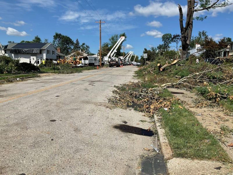 Fort Washington Tornado 6 Why I Joined a Tornado Clean Up Chainsaw Gang MyFixitUpLife Suburban street littered with fallen branches and debris after a storm utility bucket trucks and crews repairing power lines in the distance quintessential scene of storm recovery MyFixitUpLife