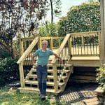 IMG 5857 7 Wood Deck Building Myths Debunked By a Pro MyFixitUpLife MyFixitUpLife Man in teal shirt and gray pants poses on a newly built wooden outdoor staircase beside a house MyFixitUpLife