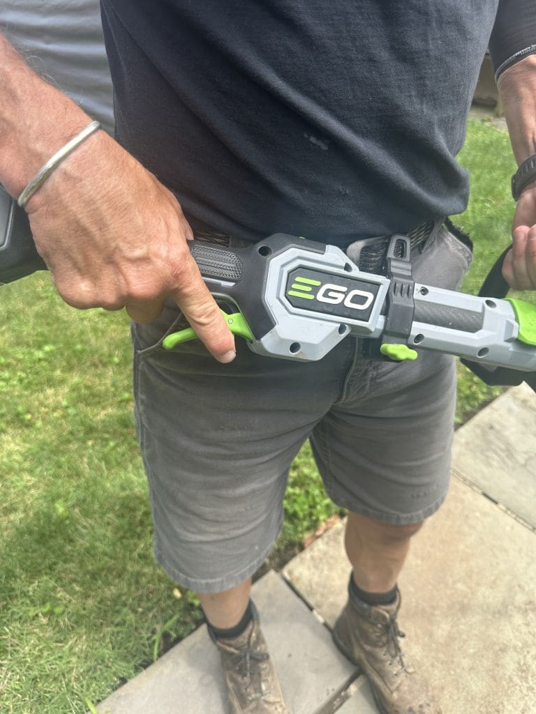 EGO String Trimmer switch Should You Try an eGo String Trimmer Maybe not MyFixitUpLife MyFixitUpLife Man in a dark T shirt and gray shorts points at a gray and green EGO tool holster attached to his waist outdoors MyFixitUpLife