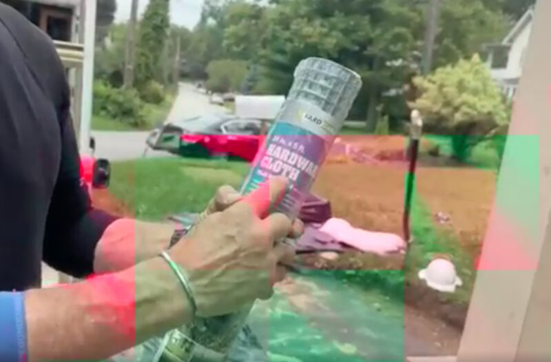 Hardware Cloth How Do I Stop Animals From Dying Under My Deck MyFixitUpLife MyFixitUpLife Person wearing pink gloves holds an aerosol spray can outdoors in a suburban yard MyFixitUpLife