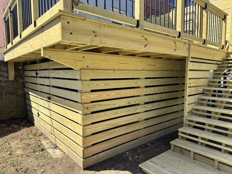 IMG 4069 How Do I Stop Animals From Dying Under My Deck MyFixitUpLife MyFixitUpLife Under deck storage area built with light wooden planks forming stacked horizontal walls a wooden staircase and railing lead up to the deck above MyFixitUpLife